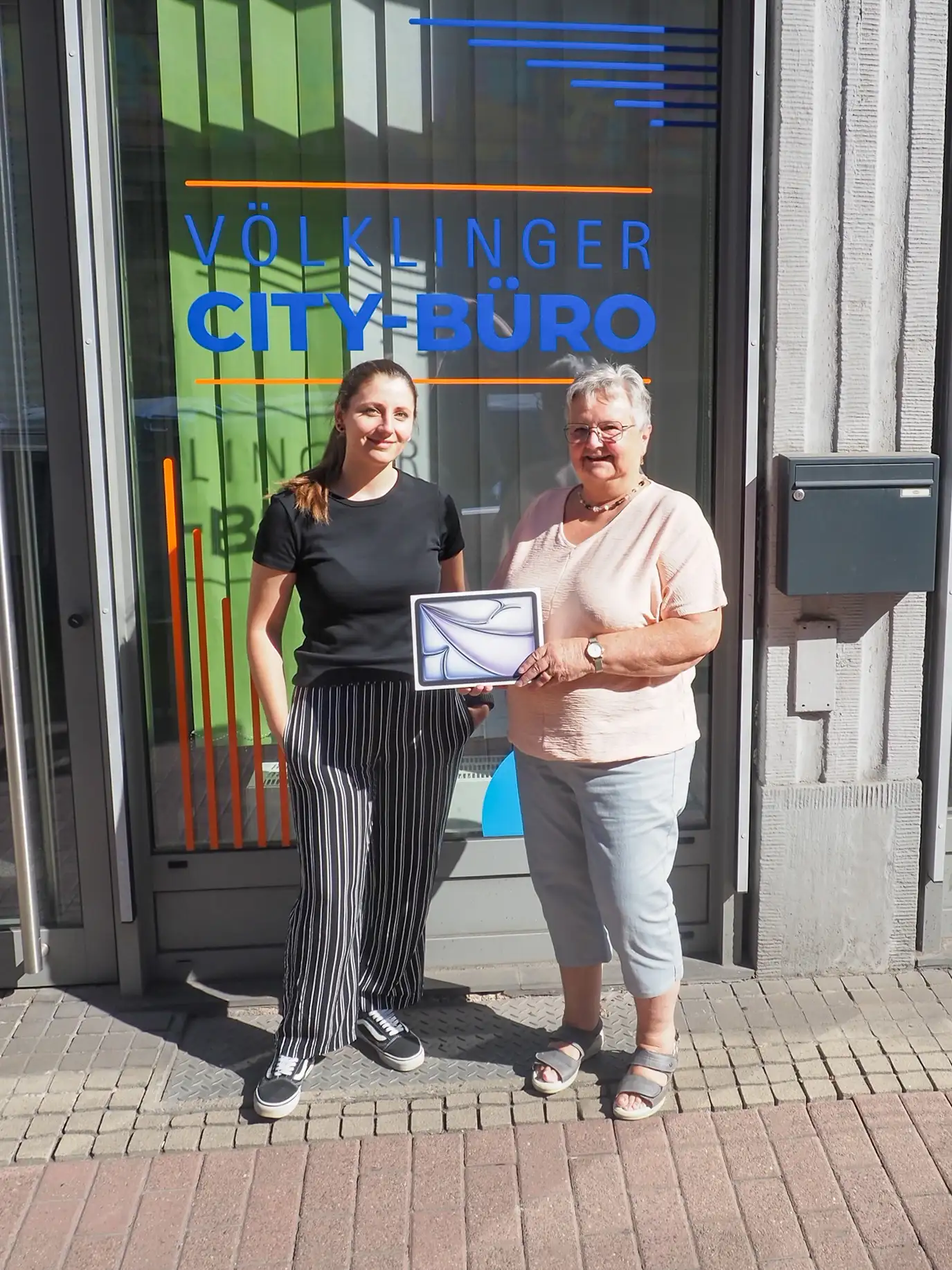 Projektleiterin Rabea Hoffmann überreicht Agnes Klemens den Hauptpreis des City Bingo Gewinnspiels, ein iPad Air.